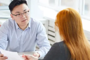 Employee holding a paper and looking at employer across the table as she points to it with a pen.