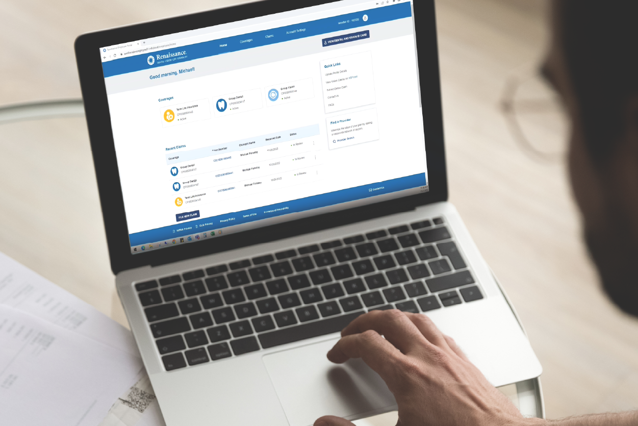 A person looks at a benefits portal on a laptop with benefits paperwork spread out on the desk.
