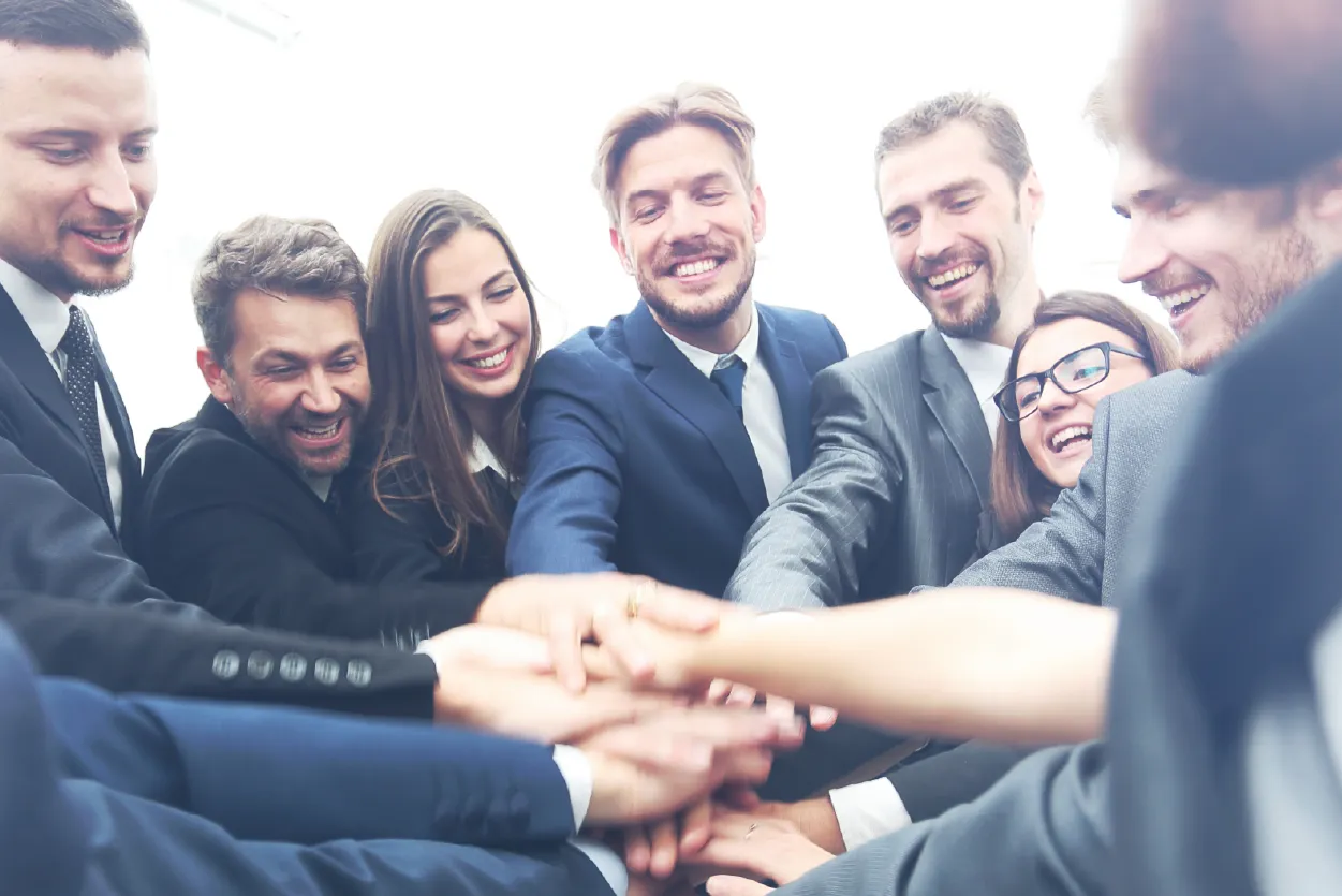Group of business professionals, both men and women, standing in a circle with their hands in the middle stacked together.