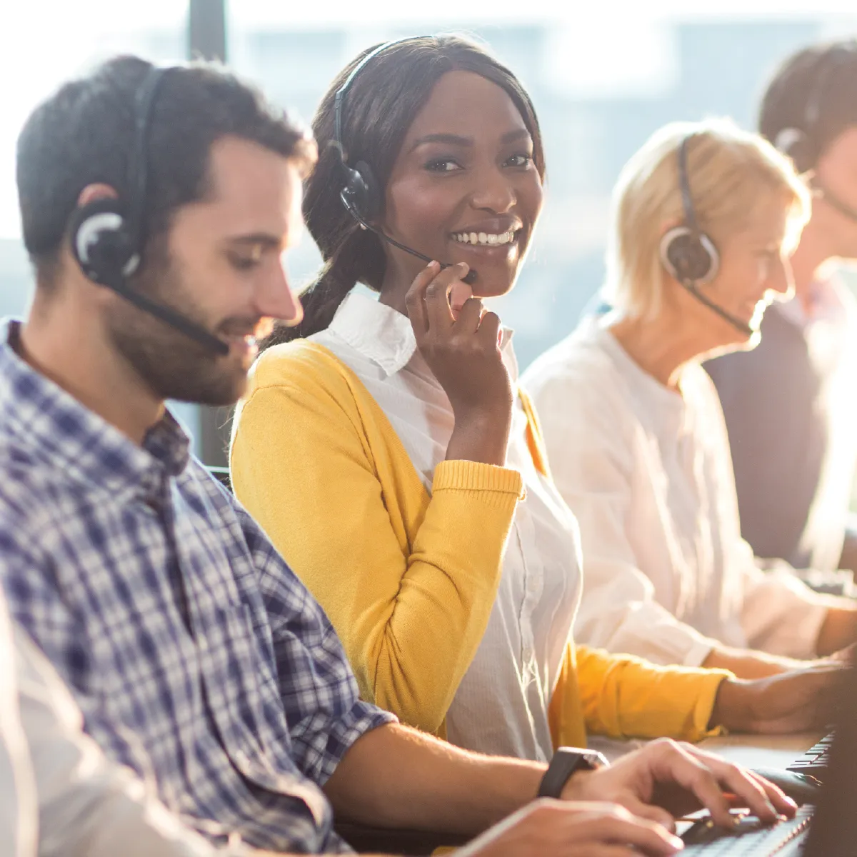 A group of employees with headsets on. One woman is looking at the camera smiling.