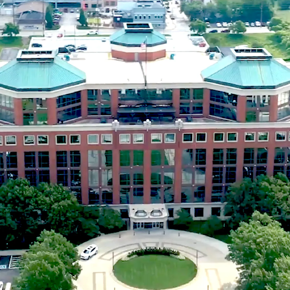 Aerial view of a red brick office building with a green roof, numerous windows, and a circular driveway in front.