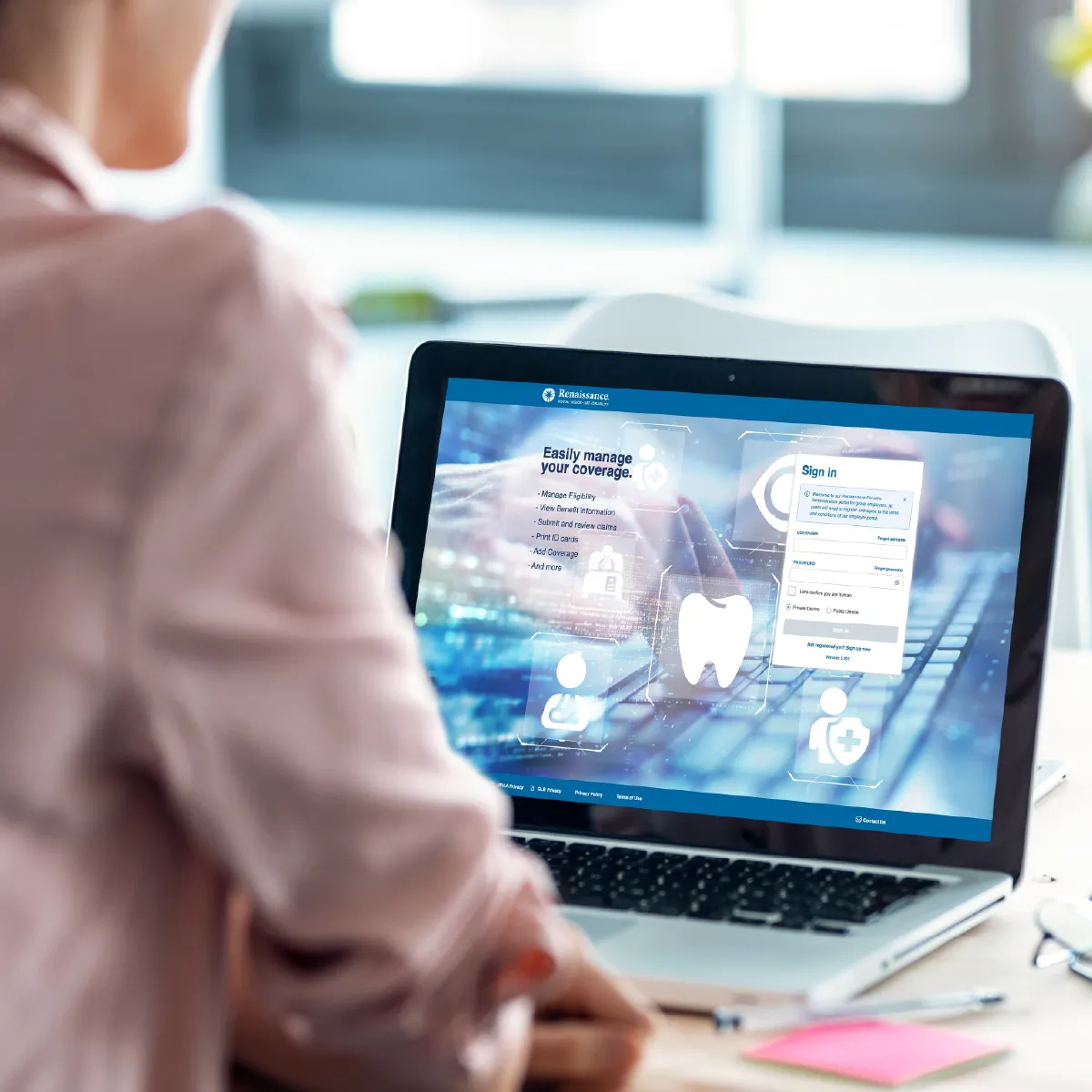 A woman in a pink blazer with her back to the camera is looking at an employer portal on a laptop.