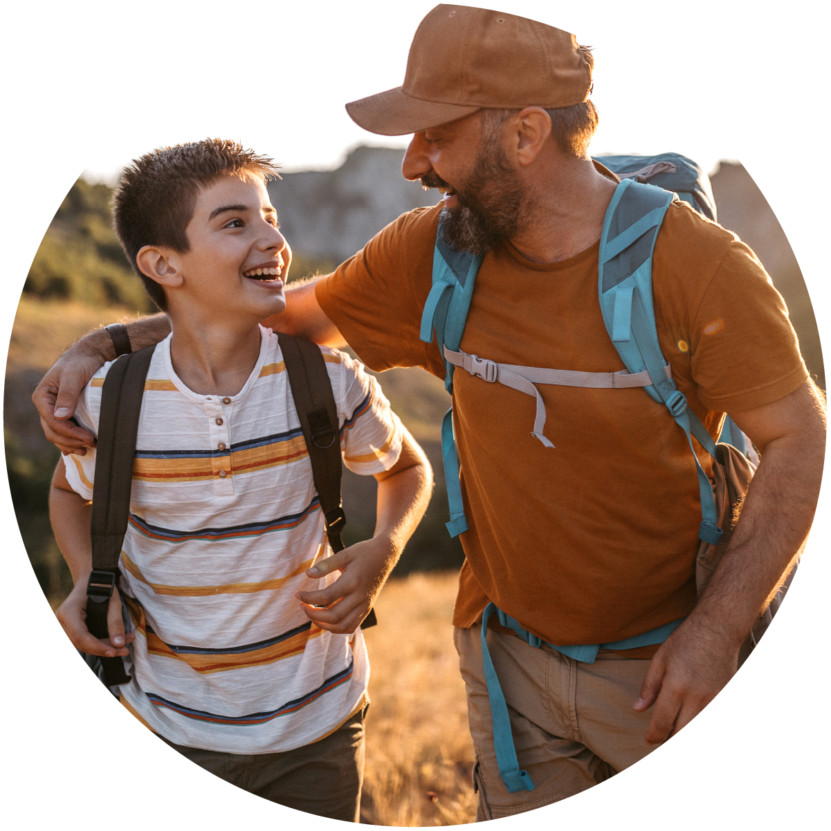 Father with arm around his young son's shoulder, both wearing backpacks while standing outside together.