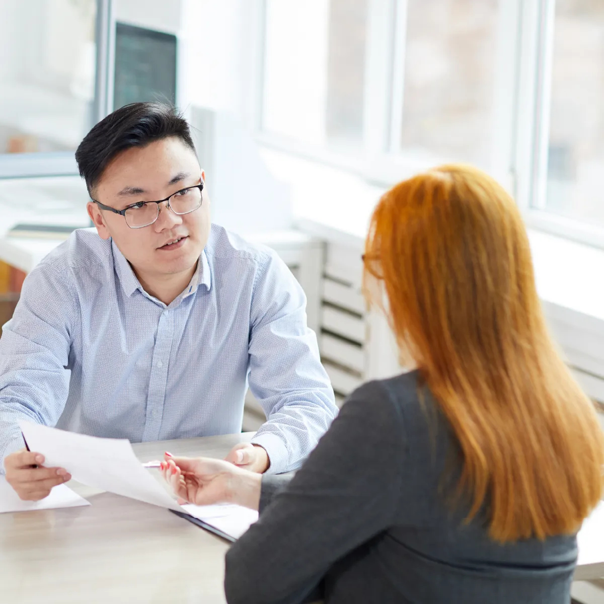 Employee holding a paper and looking at employer across the table as she points to it with a pen.