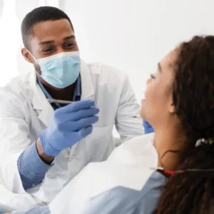 Woman in a dentist's chair with her back to the camera as a masked dentist holds a dental tool beside her.