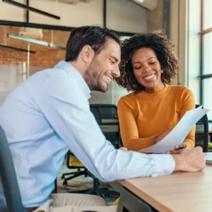 A man and a woman sitting at a desk in an office, reviewing documents together.
