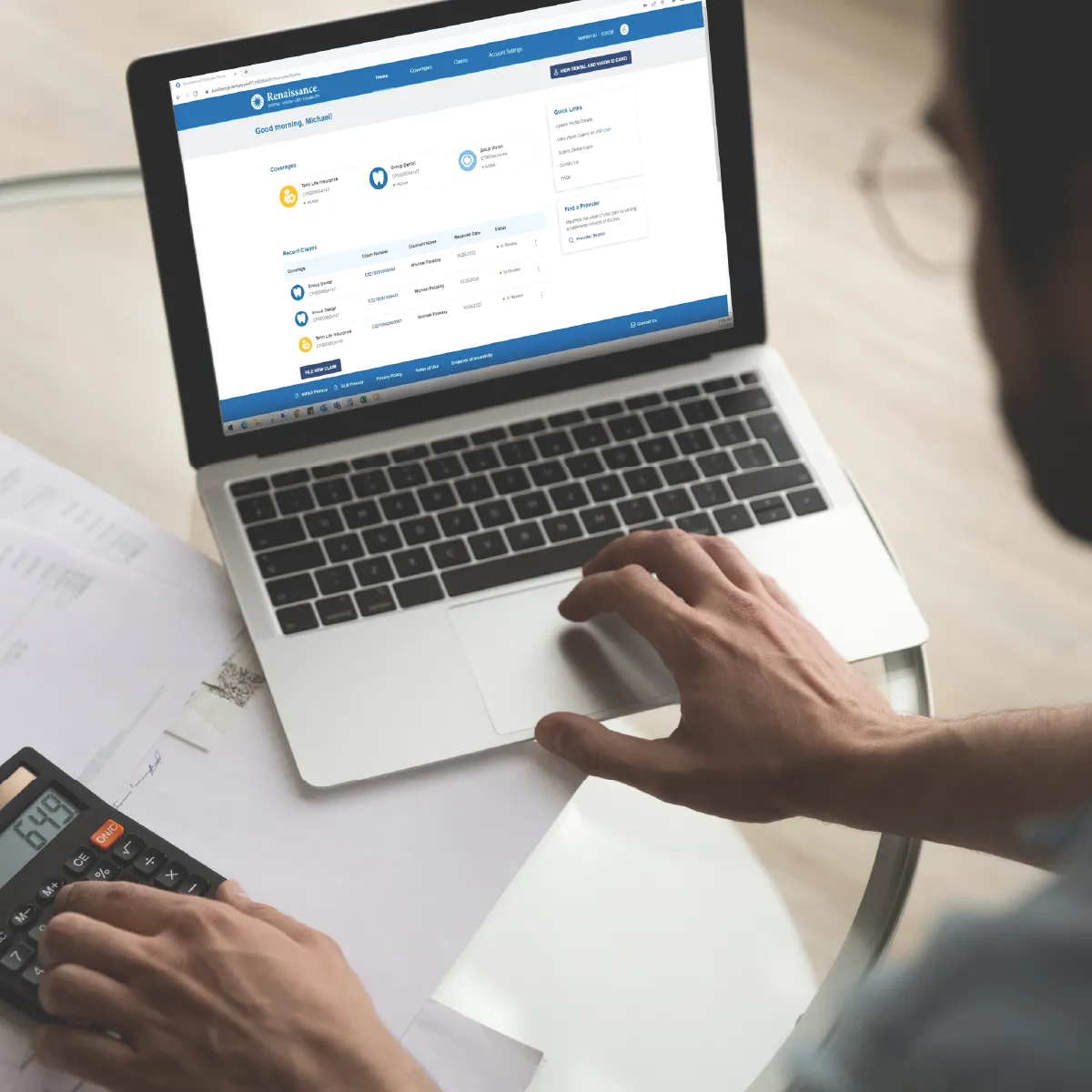 A person looks at a benefits portal on a laptop with benefits paperwork spread out on the desk.