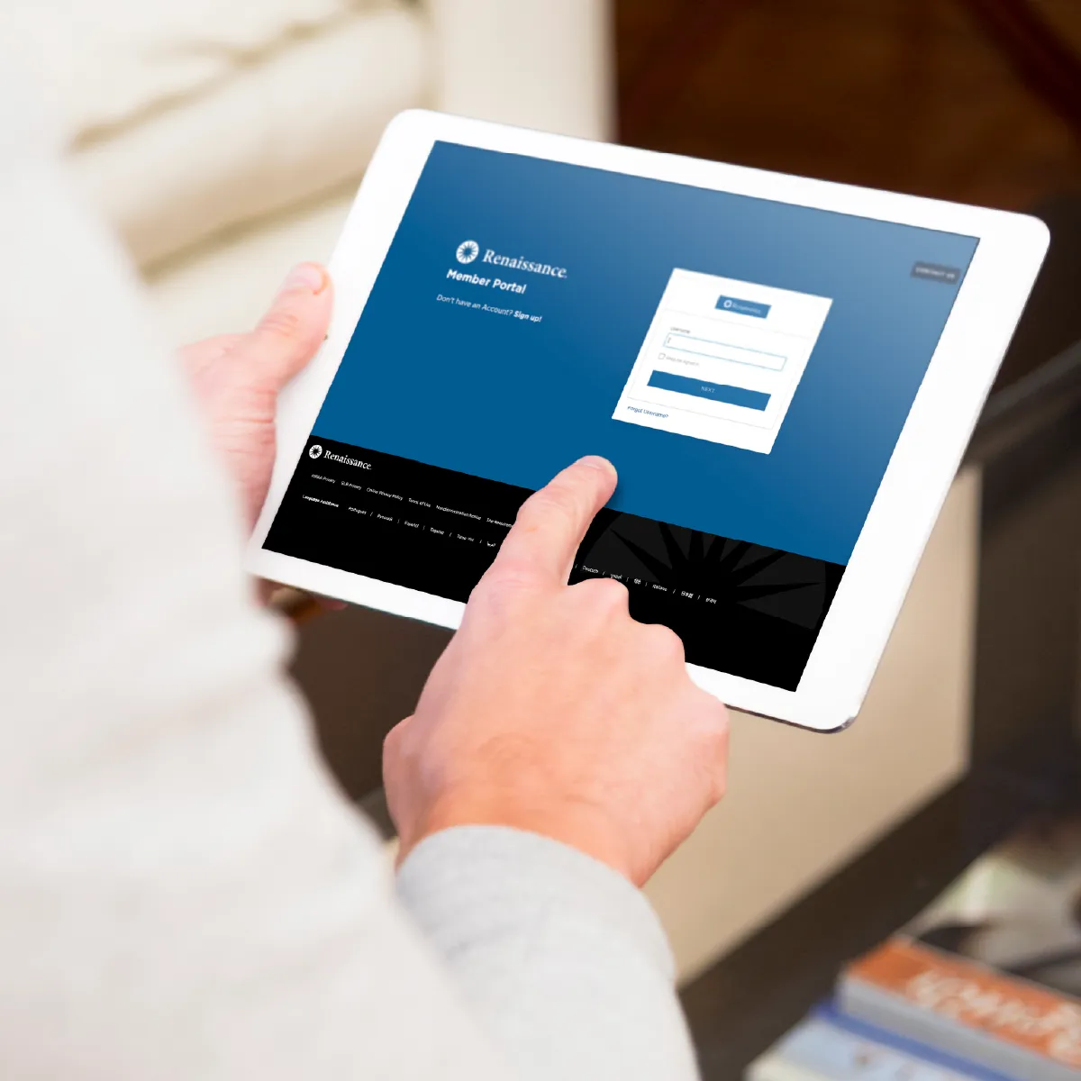 Close-up of hands holding a tablet displaying a member portal login screen, with a finger touching the screen.