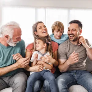 Multigenerational Caucasian family with grandfather, mom, dad and young daughter and son sitting on a couch smiling.