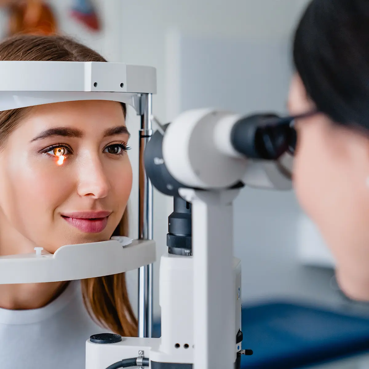 Patient rests her head in an ophthalmoscope while an eye doctor looks conducts an eye exam.