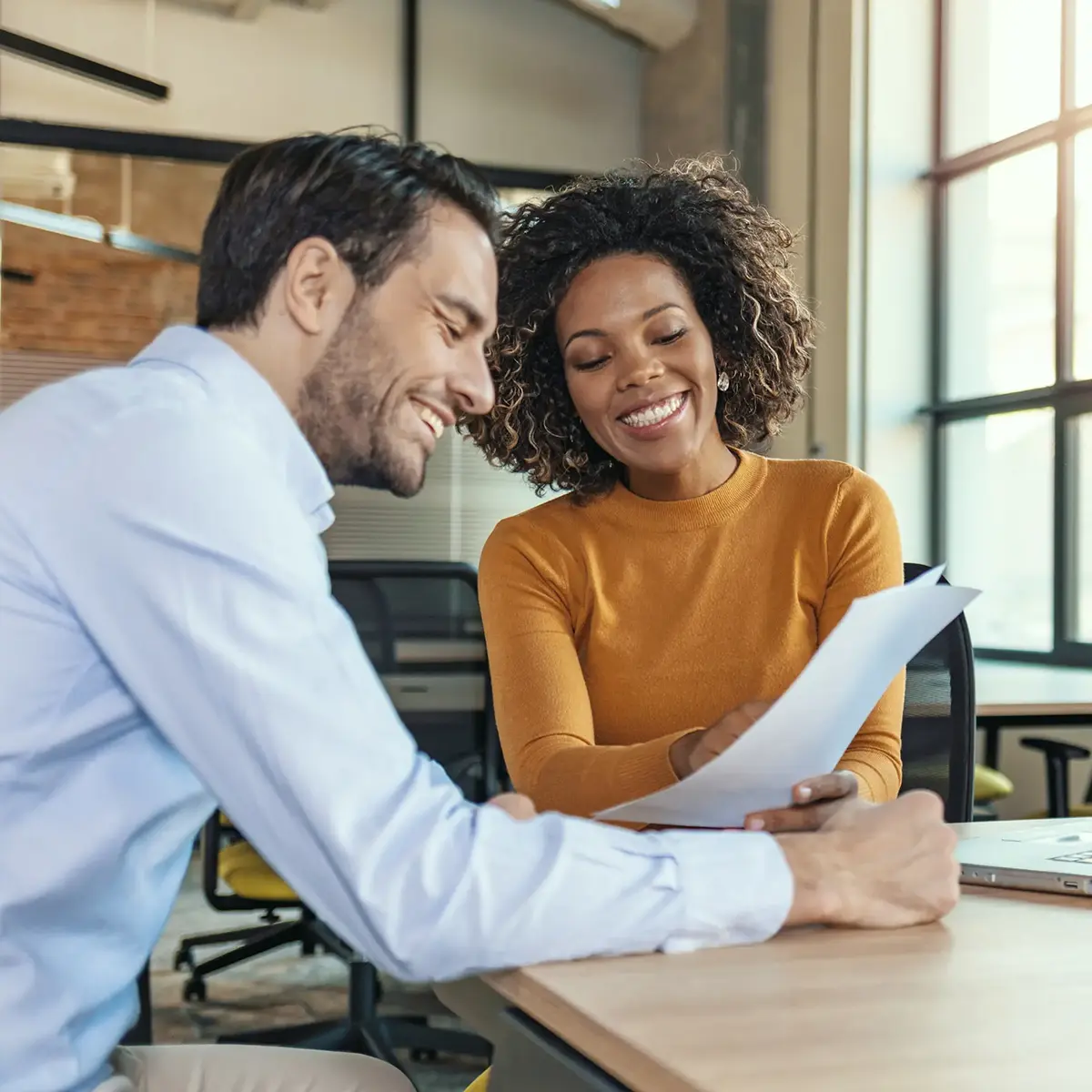 A man and a woman sitting at a desk in an office, reviewing documents together.
