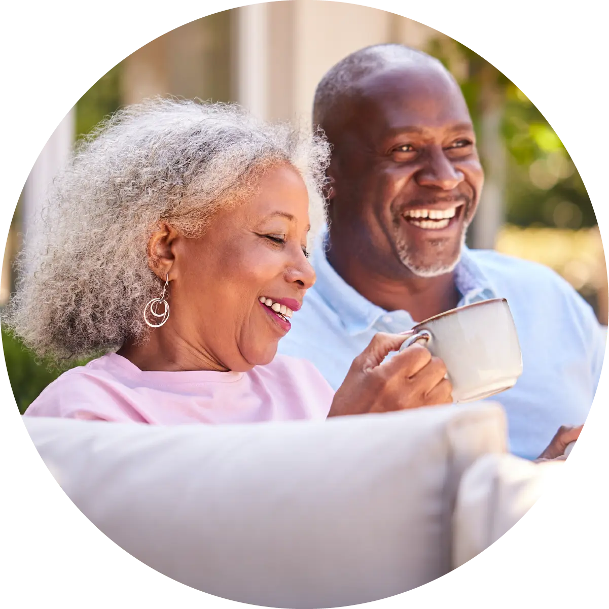 Senior man and senior woman sitting on the couch smiling. Woman is holding a coffee cup.
