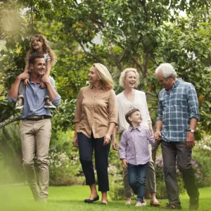 Multigenerational family taking a walk. Daughter is sitting on Dad's shoulder and son is holding Grandpa's hand.