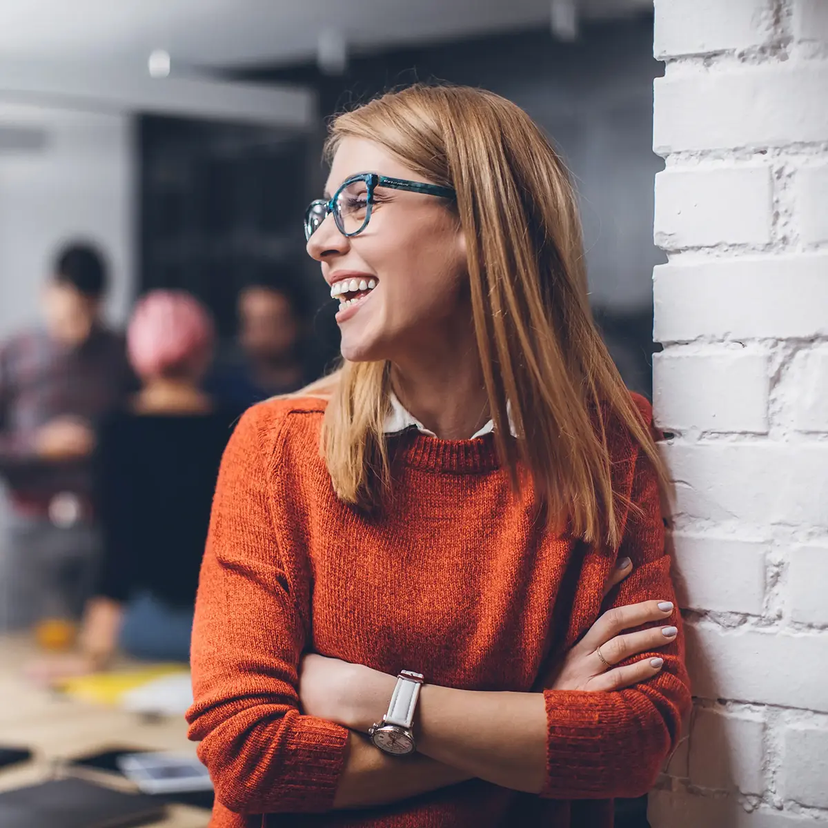 Smiling woman looking off to the left while leaning against a brick wall in a doorway.
