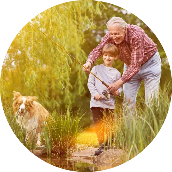 Grandpa helping grandson fish off the shore with a fishing rod. A dog is sitting next to them.