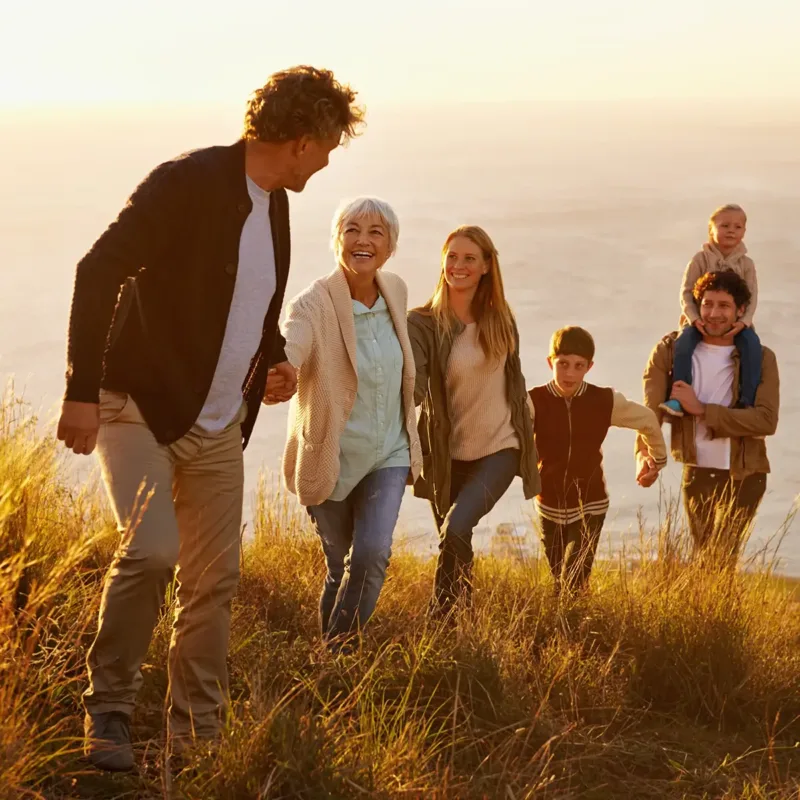 A multigenerational family climbing a hill, holding hands. One son is on his dad's shoulders.
