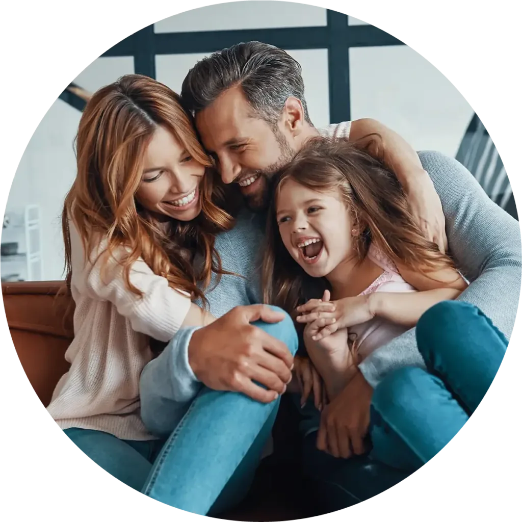 Family of three—mother, father and daughter—sitting on a couch laughing together.