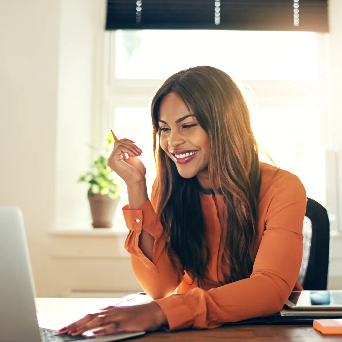 Smiling young woman looking at her tablet while holding a pencil and typing on the keyboard.