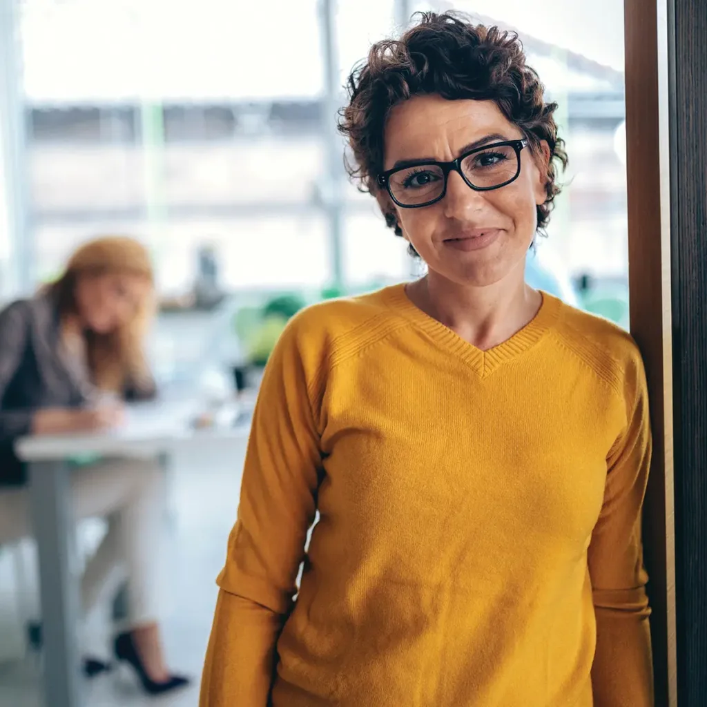 Smiling woman stands in her office doorway, leaning against the door frame with her hands relaxed at her sides.