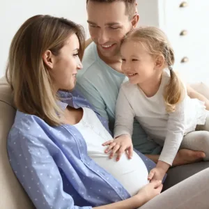 Smiling young couple with their child who is touching the mom's pregnant belly.