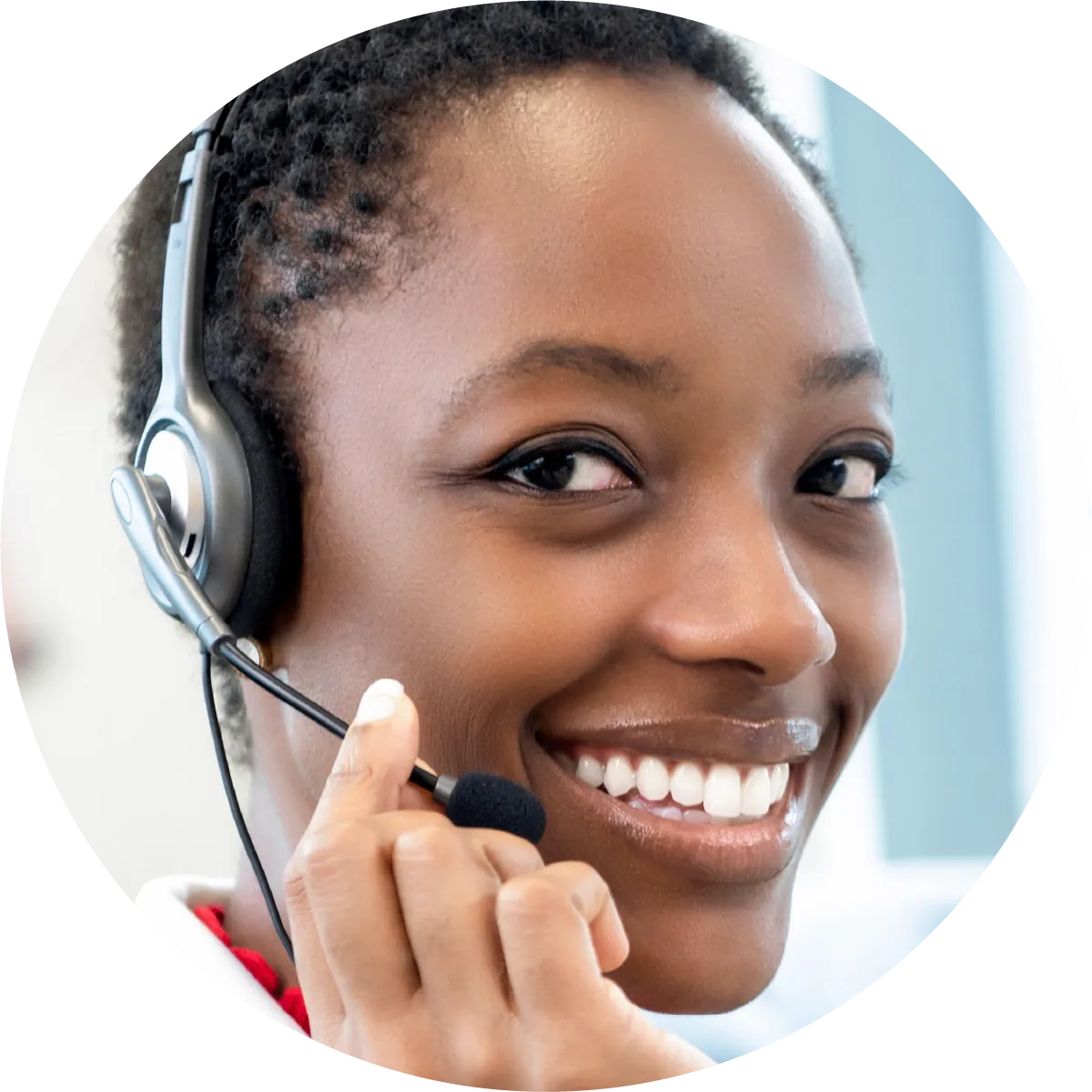 smiling woman with short dark hair wears a headset, looking directly at the viewer in a call center environment