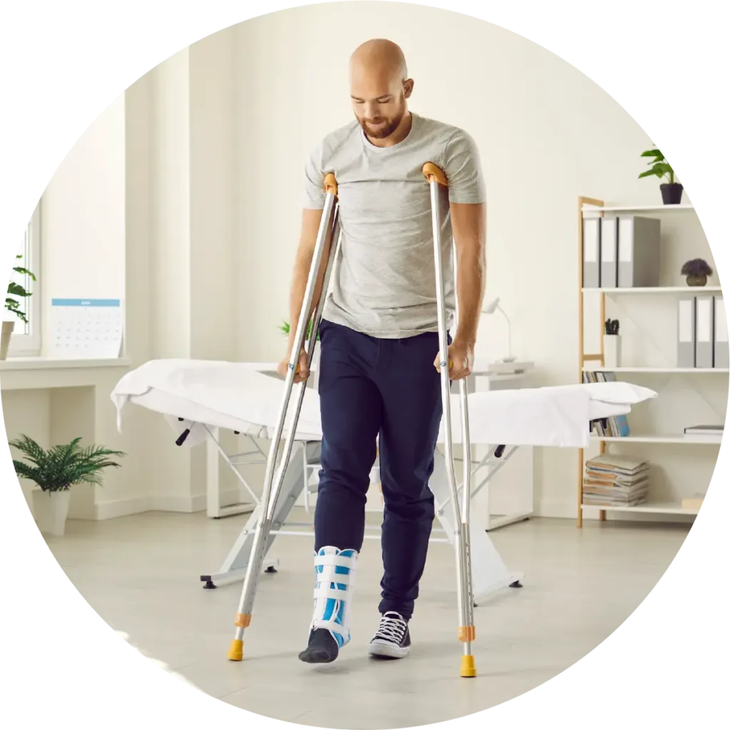 A man standing on crutches with an ankle and lower leg brace in a doctor's exam room.