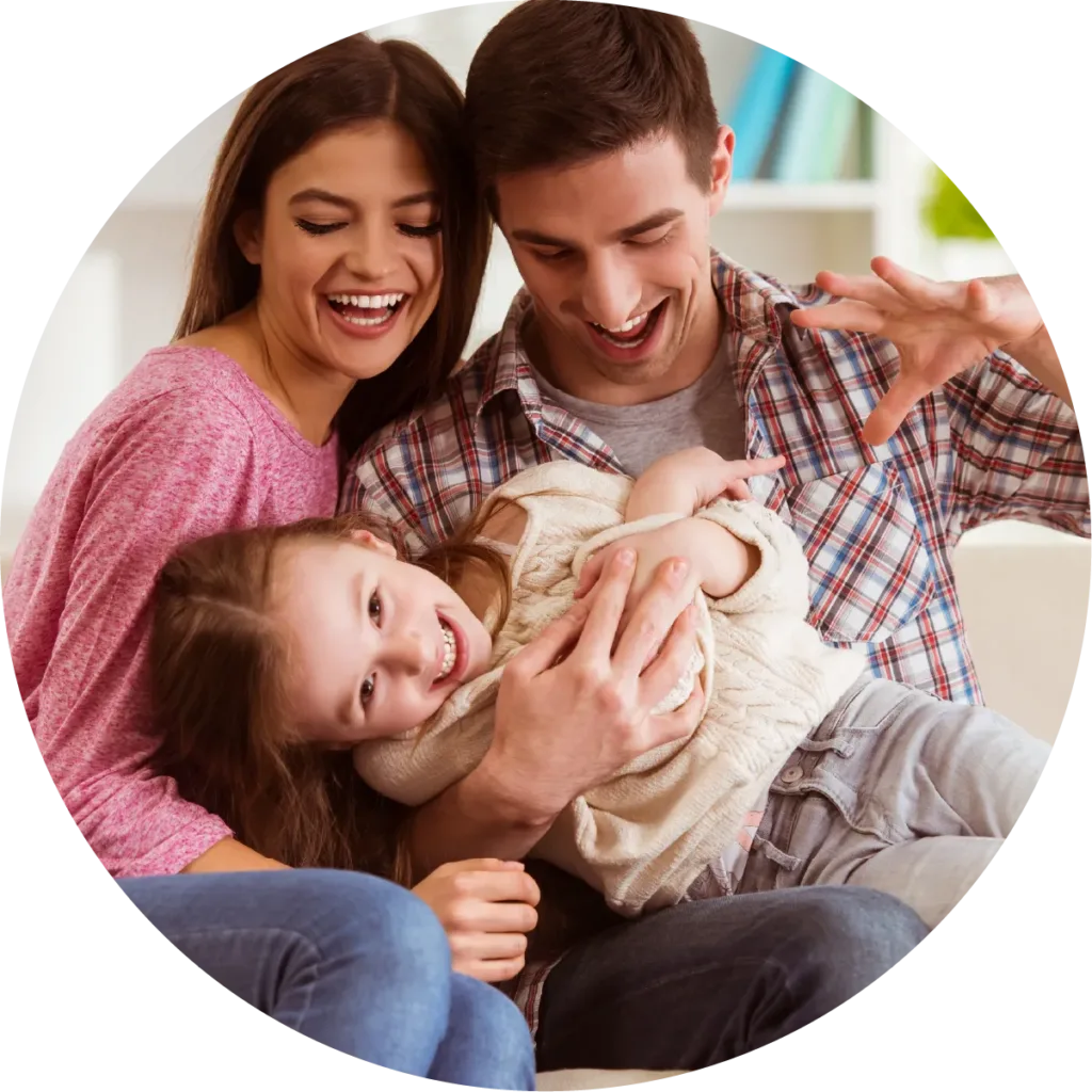 Mother and father sitting on the couch together laughing. Daughter is laying on Dad's lap.