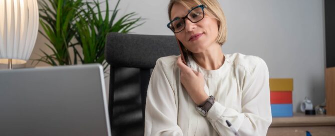 HR manager talks on the phone while reviewing paperwork at their desk.