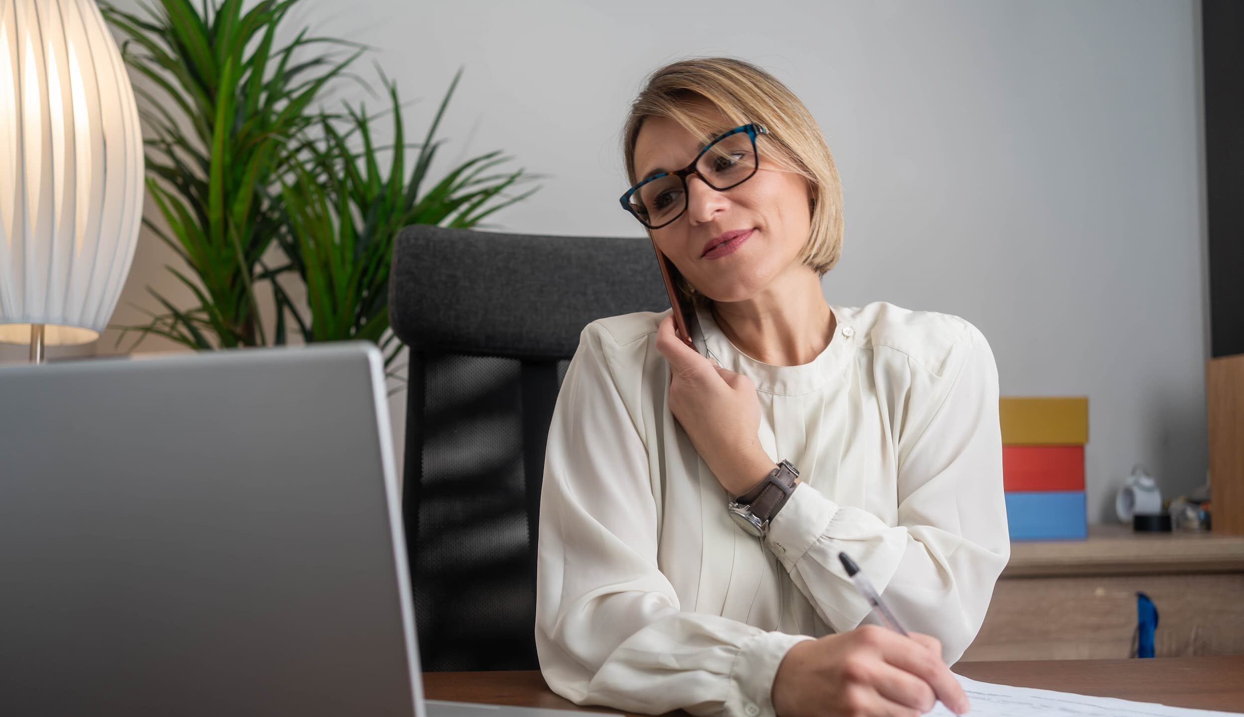 HR manager talks on the phone while reviewing paperwork at their desk.
