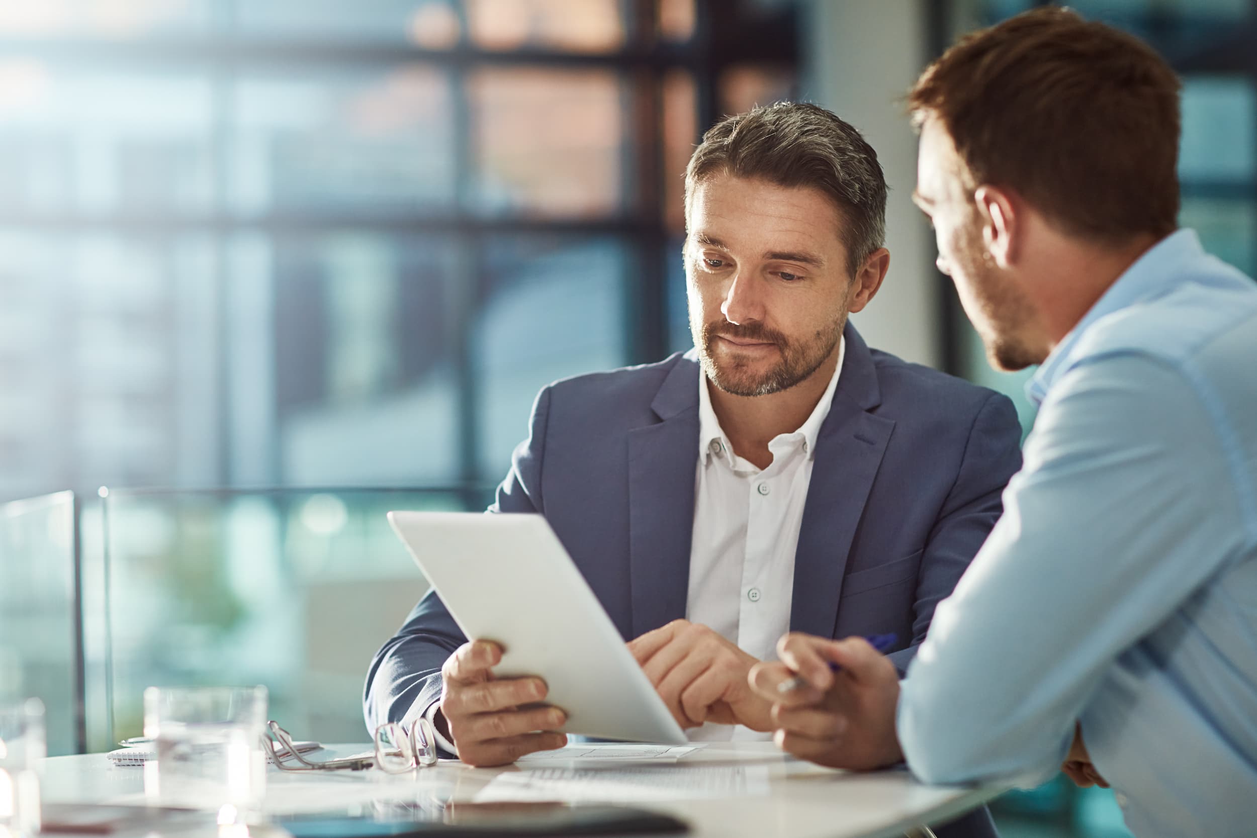 Two professionals in a modern office discussing information displayed on a tablet during a meeting.