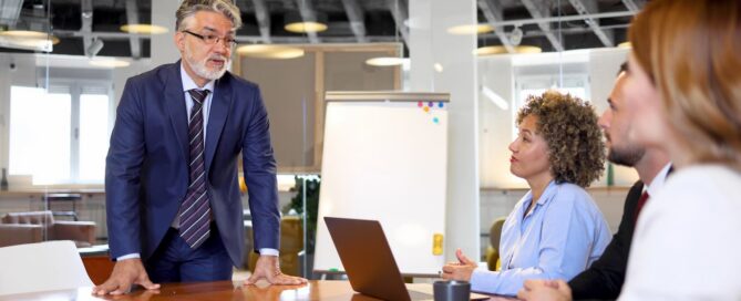 Business leader speaking to colleagues around a conference table during a team meeting.