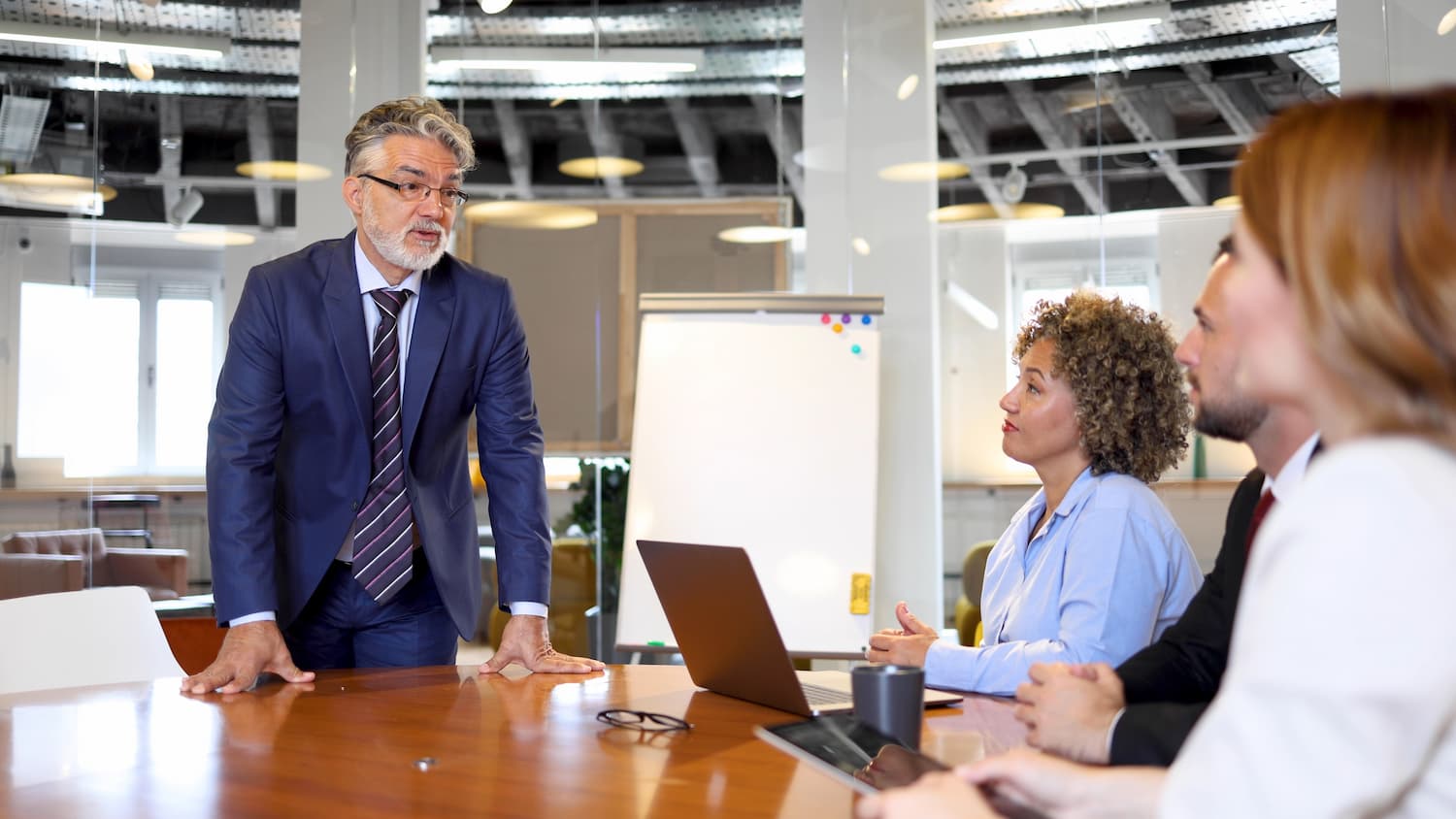 AdobeStock_990723402 Business leader speaking to colleagues around a conference table during a team meeting.