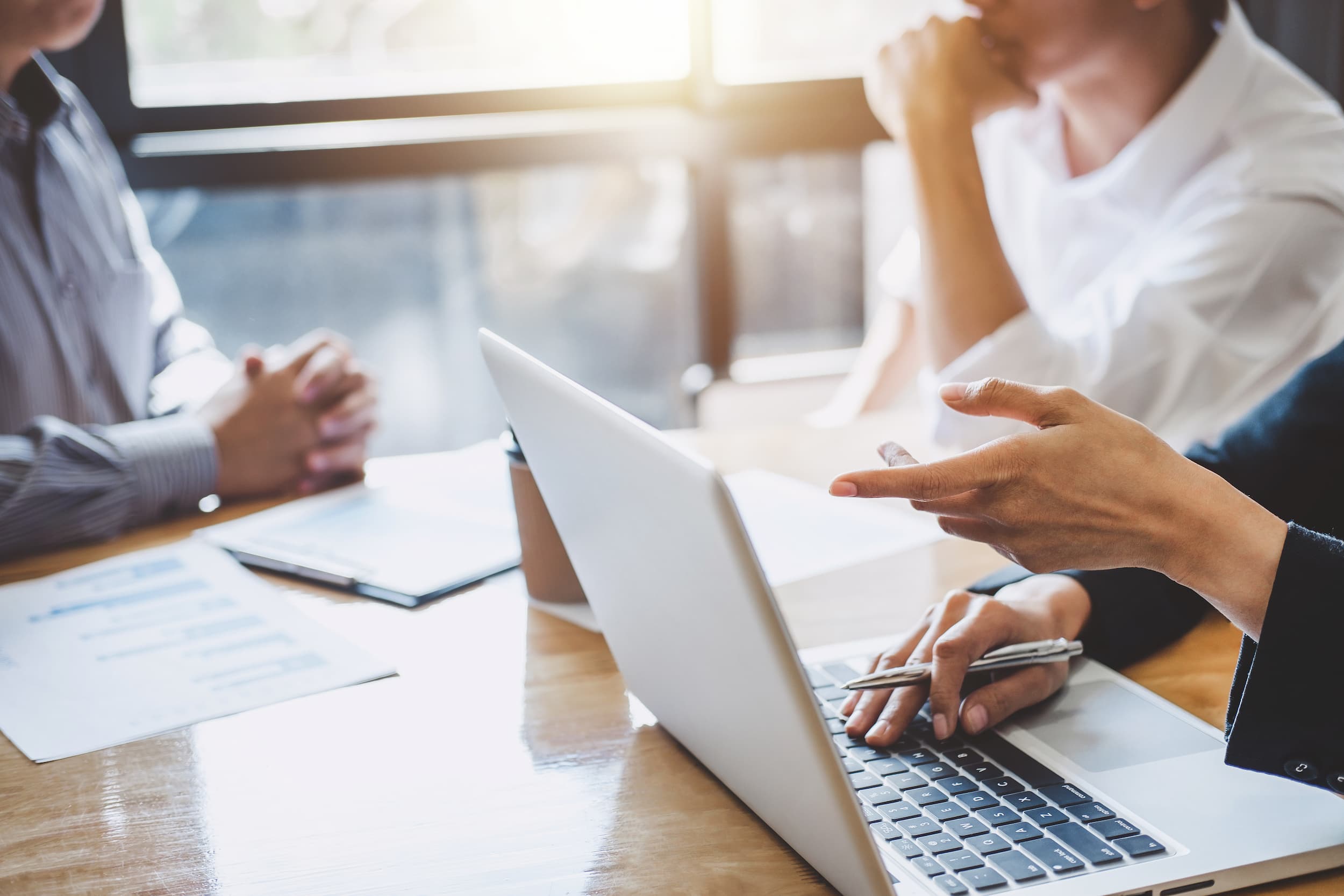Two professionals meeting at a table with a laptop, documents, and a tablet during a workplace discussion.