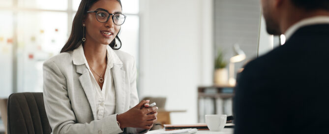 HR professional speaking with a client across a desk during an office meeting.