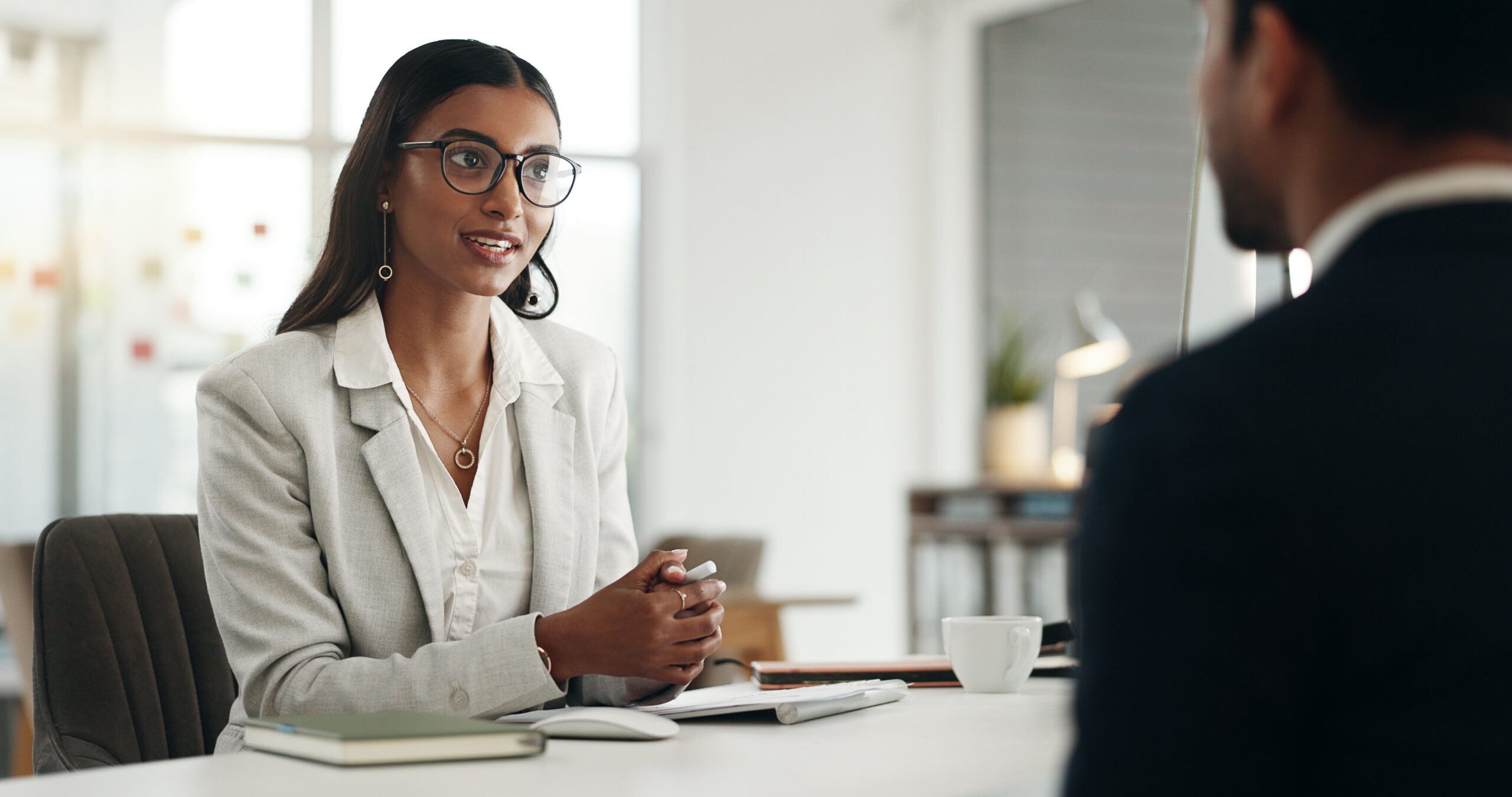 HR professional speaking with a client across a desk during an office meeting.