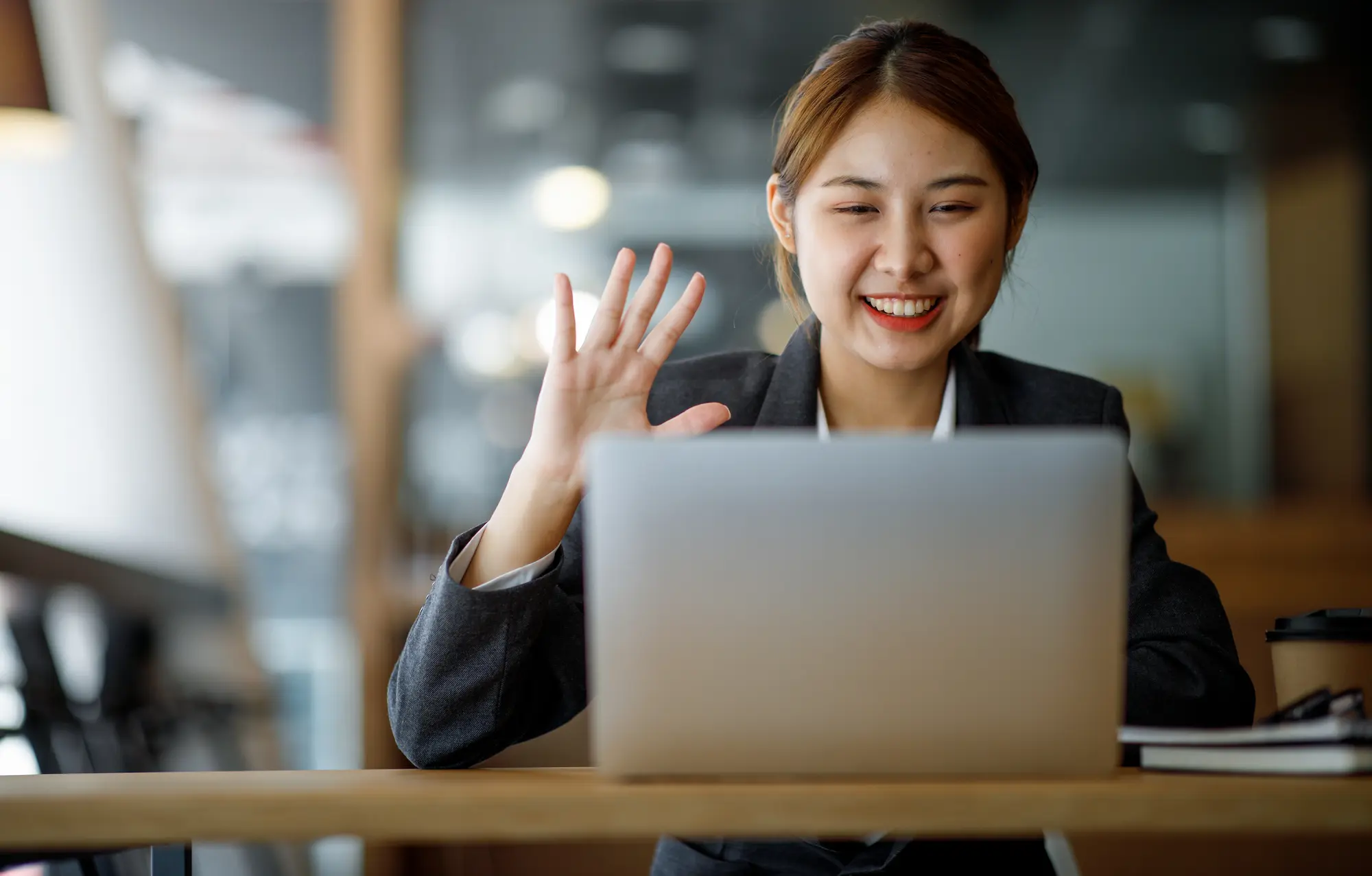 Woman in a suit waving at a virtual meeting